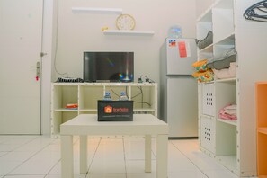 A hotel room with a television on a stand, a small table with a travelio sign, and a refrigerator with a water dispenser.