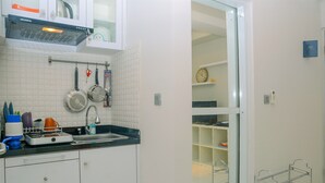 A compact kitchen with white cabinets, a black countertop, and a dish rack. - City View Studio Apartment at Menteng Square (Jakarta)