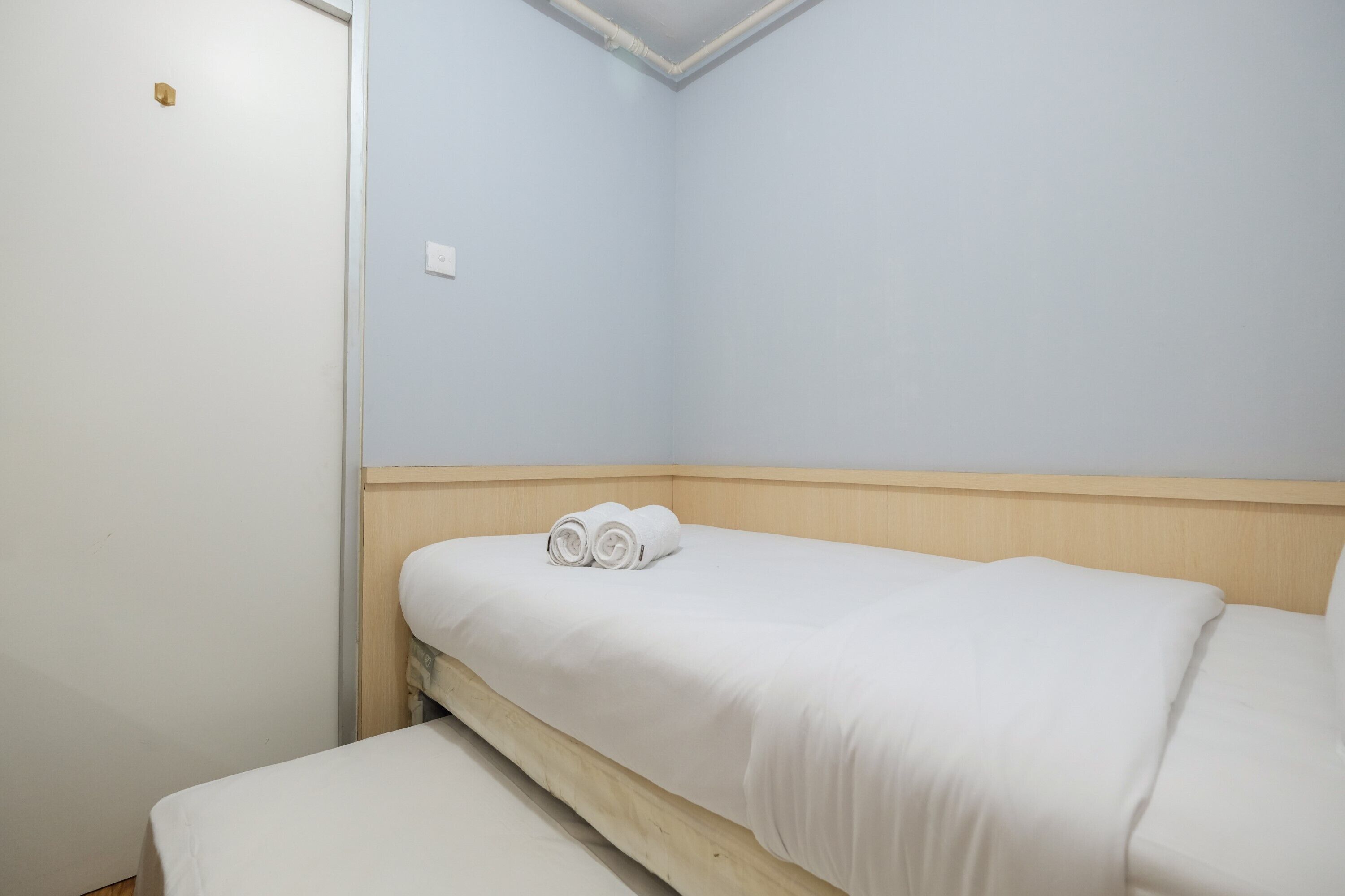 Une petite chambre avec un lit simple, une tête de lit en bois, un matelas blanc et une paire de serviettes enroulées posées sur le lit.