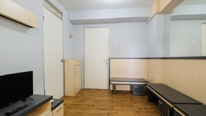 A small, well-lit room with a wooden floor, a flat-screen TV, a bench, and a small cabinet. - Cozy 2BR Apartment at Gading Nias Residences (Jakarta)