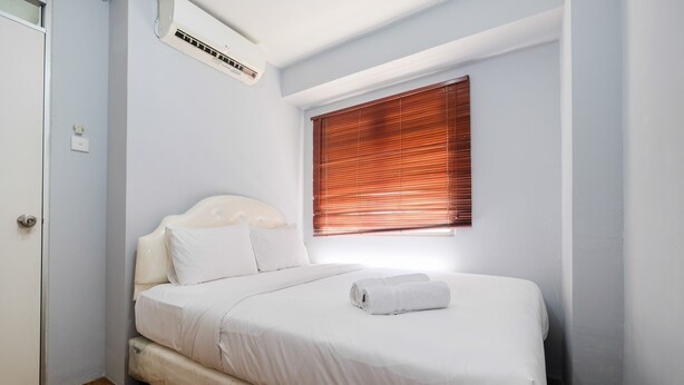A single-bed room with a wooden floor, white bedding, a window with blinds, and an air conditioning unit. - Cozy 2BR Apartment at Gading Nias Residences (Jakarta)