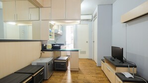 A compact kitchen with wooden cabinets, a small refrigerator, and a built-in microwave. - Cozy 2BR Apartment at Gading Nias Residences (Jakarta)