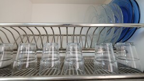 A metal rack with clear glasses and blue plates stacked on shelves. - Cozy 2BR Apartment at Gading Nias Residences (Jakarta)