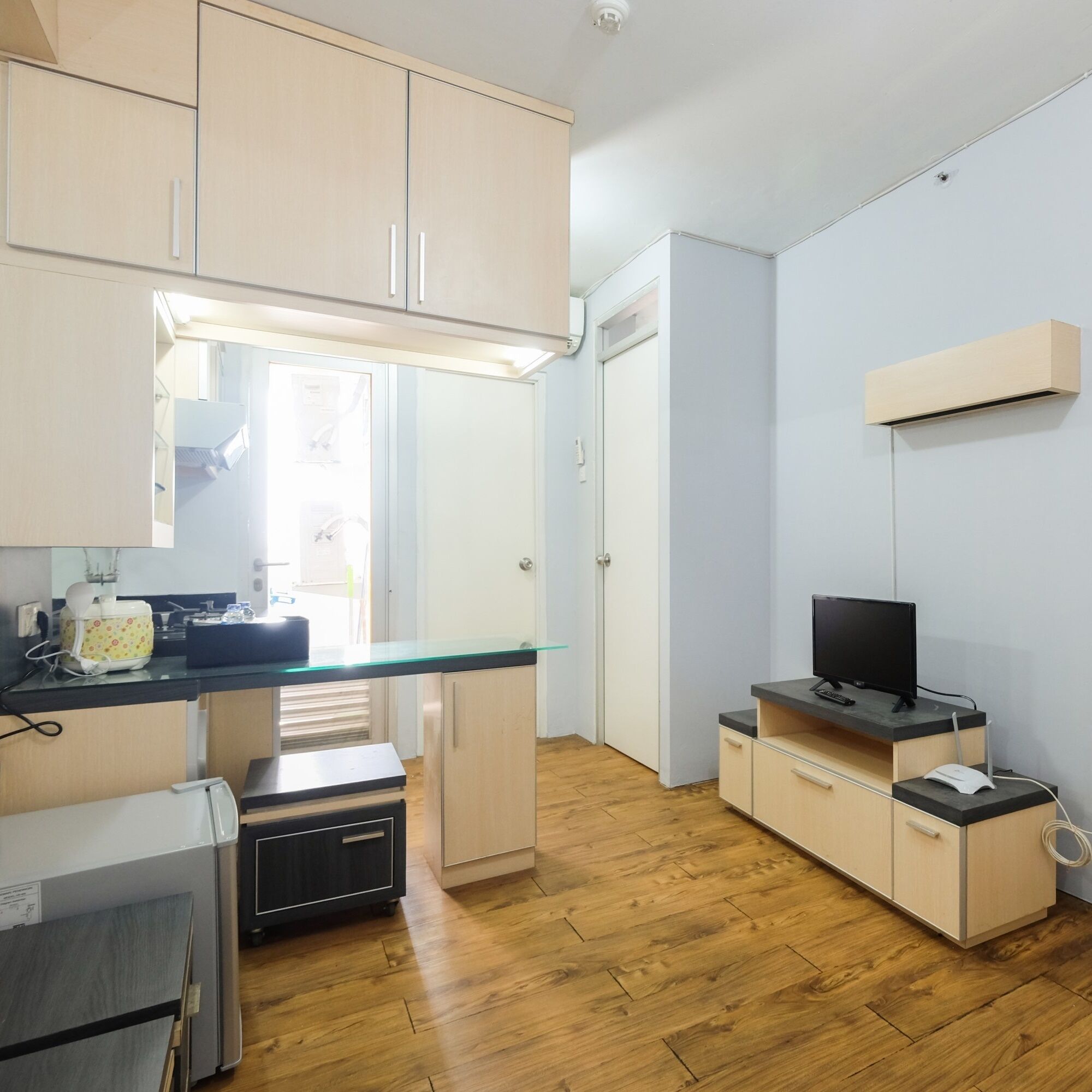 Una cocina compacta con armarios de madera, encimera de cristal y televisor integrado.