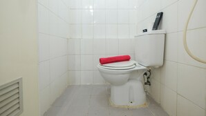 A small, white-tiled bathroom with a toilet, a red towel on the seat, and a black object on the tank. - Cozy 2BR Apartment at Gading Nias Residences (Jakarta)