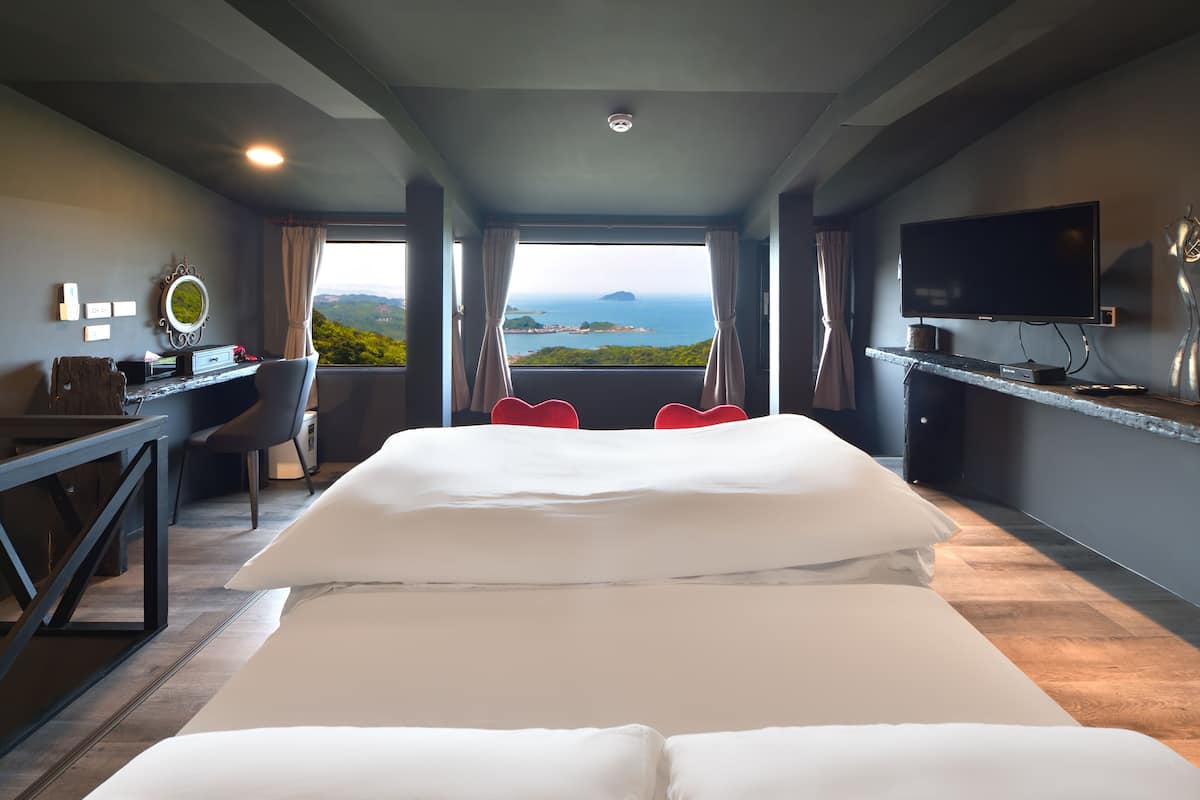 A hotel room with a large bed, a desk, a chair, a TV, and a view of the sea.