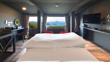 A hotel room with a large bed, a desk, a chair, a TV, and a view of the sea.
