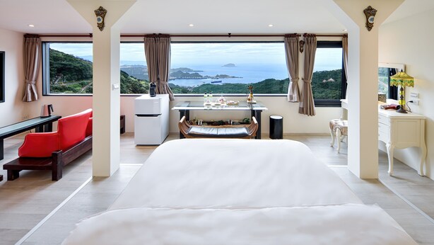 A spacious bedroom with a large bed, a desk with a chair, a small table, and a view of a mountainous landscape. - Windsor's Sunlight Han-Guan (New Taipei City)