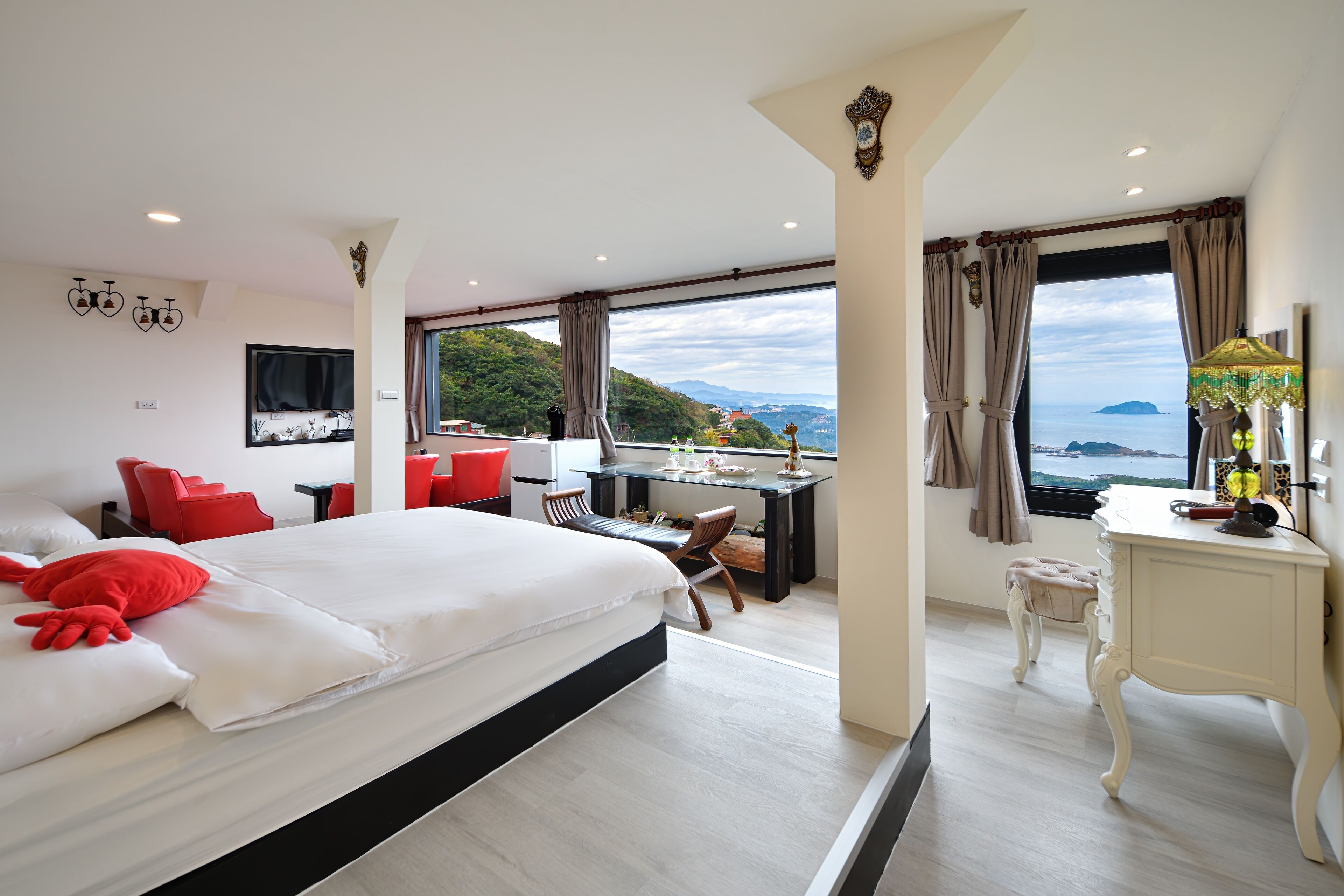 A modern bedroom with a large bed, a desk, and a view of the sea.
