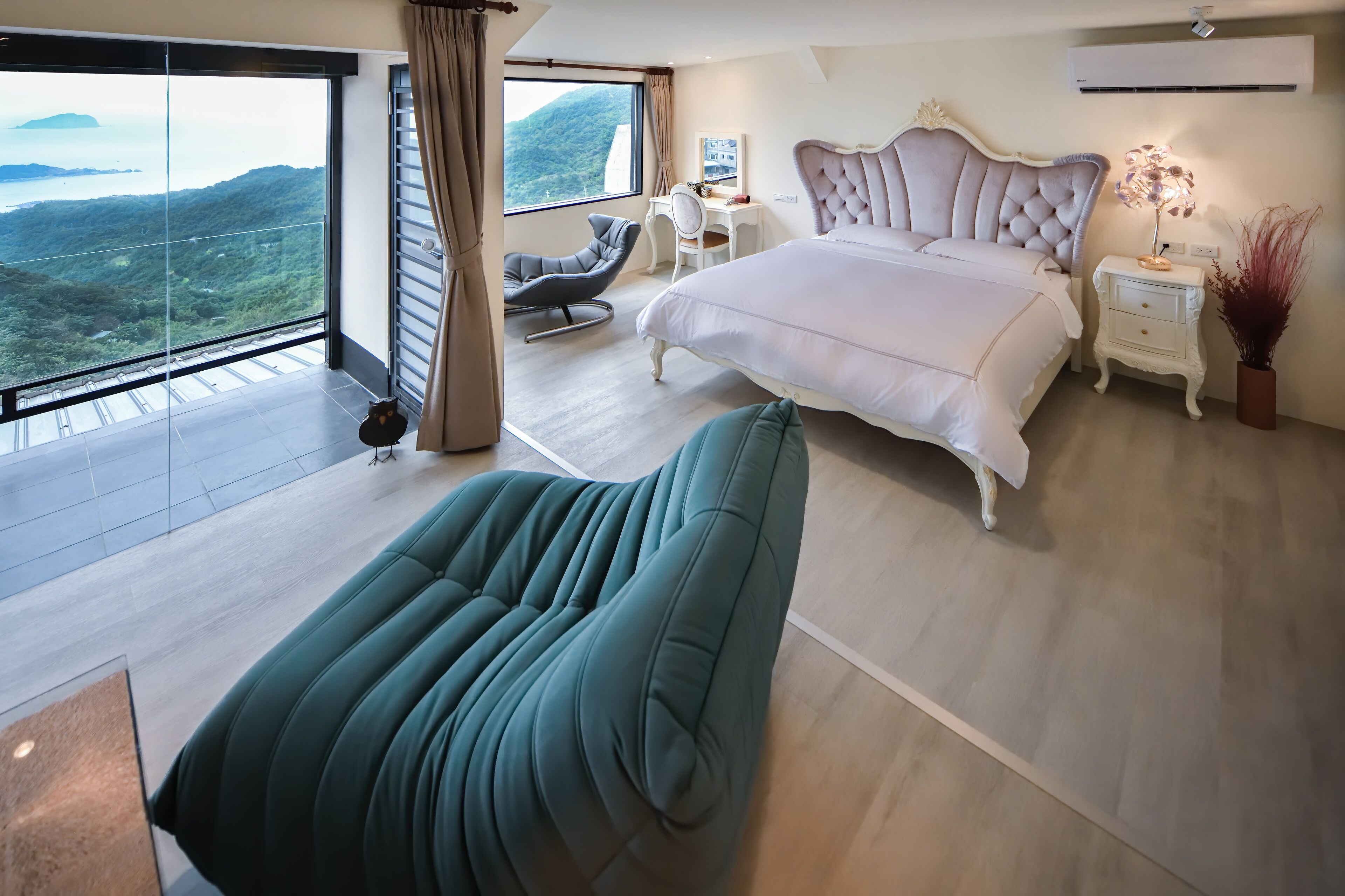 A bedroom with a large bed, a desk, a chair, and a view of the outdoors.