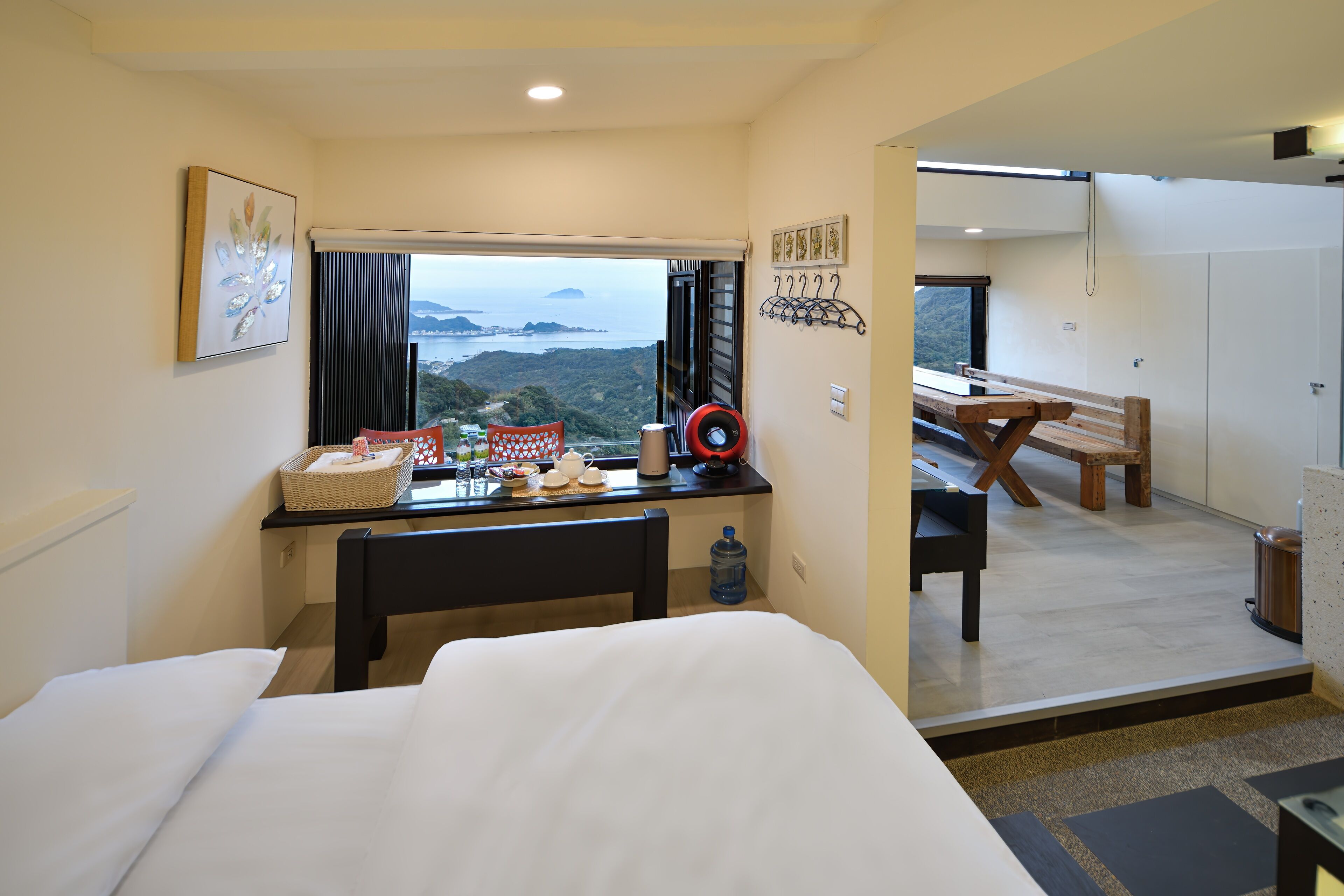 Een hotelkamer met een bed, een bureau met computer, een raam met uitzicht op zee, en een badkamer die door een geopende deur zichtbaar is.