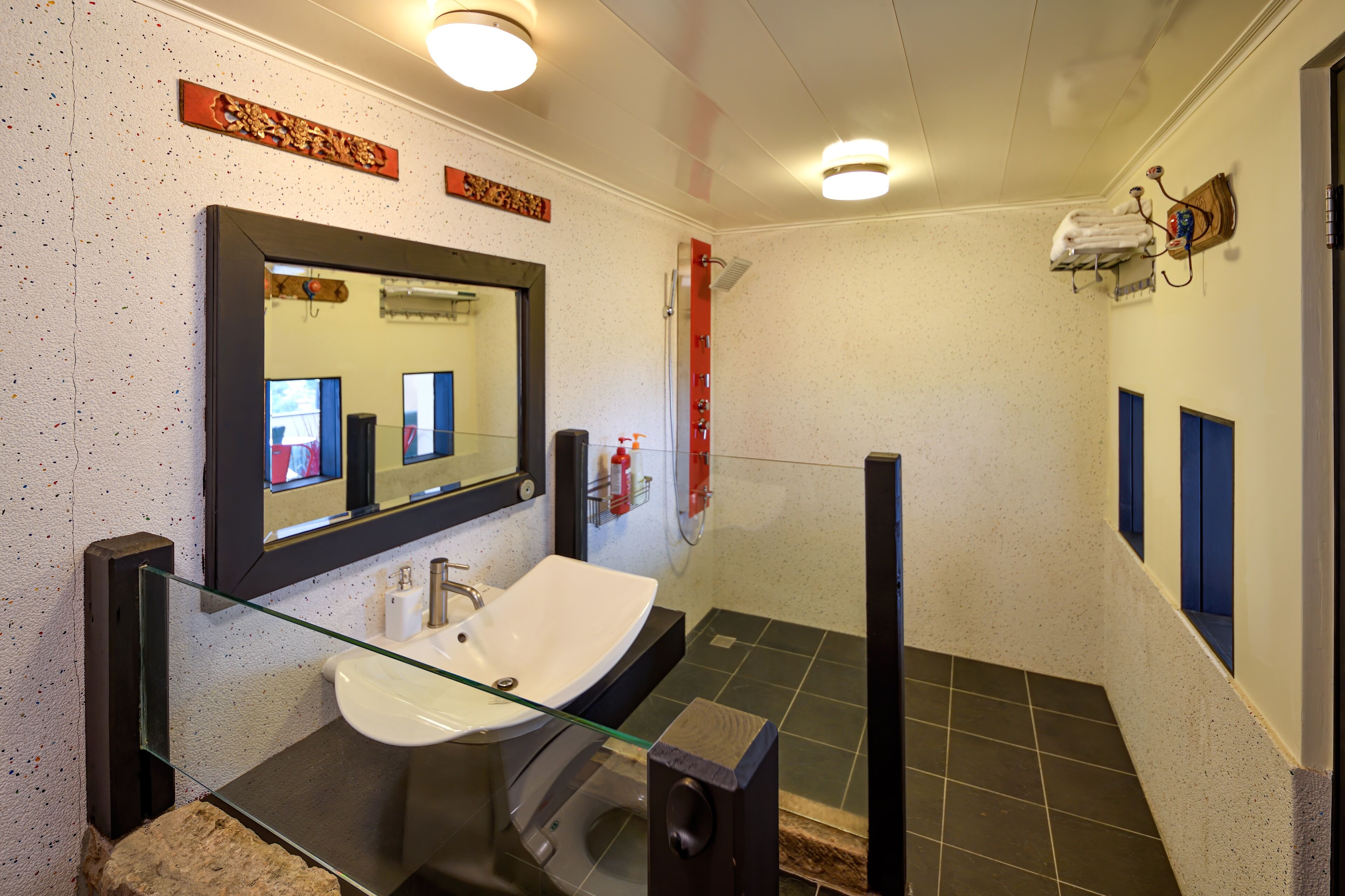Un baño moderno con lavamanos de vidrio, un espejo grande, ducha y un perchero para toallas.