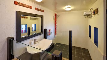 Un baño moderno con lavamanos de vidrio, un espejo grande, ducha y un perchero para toallas.