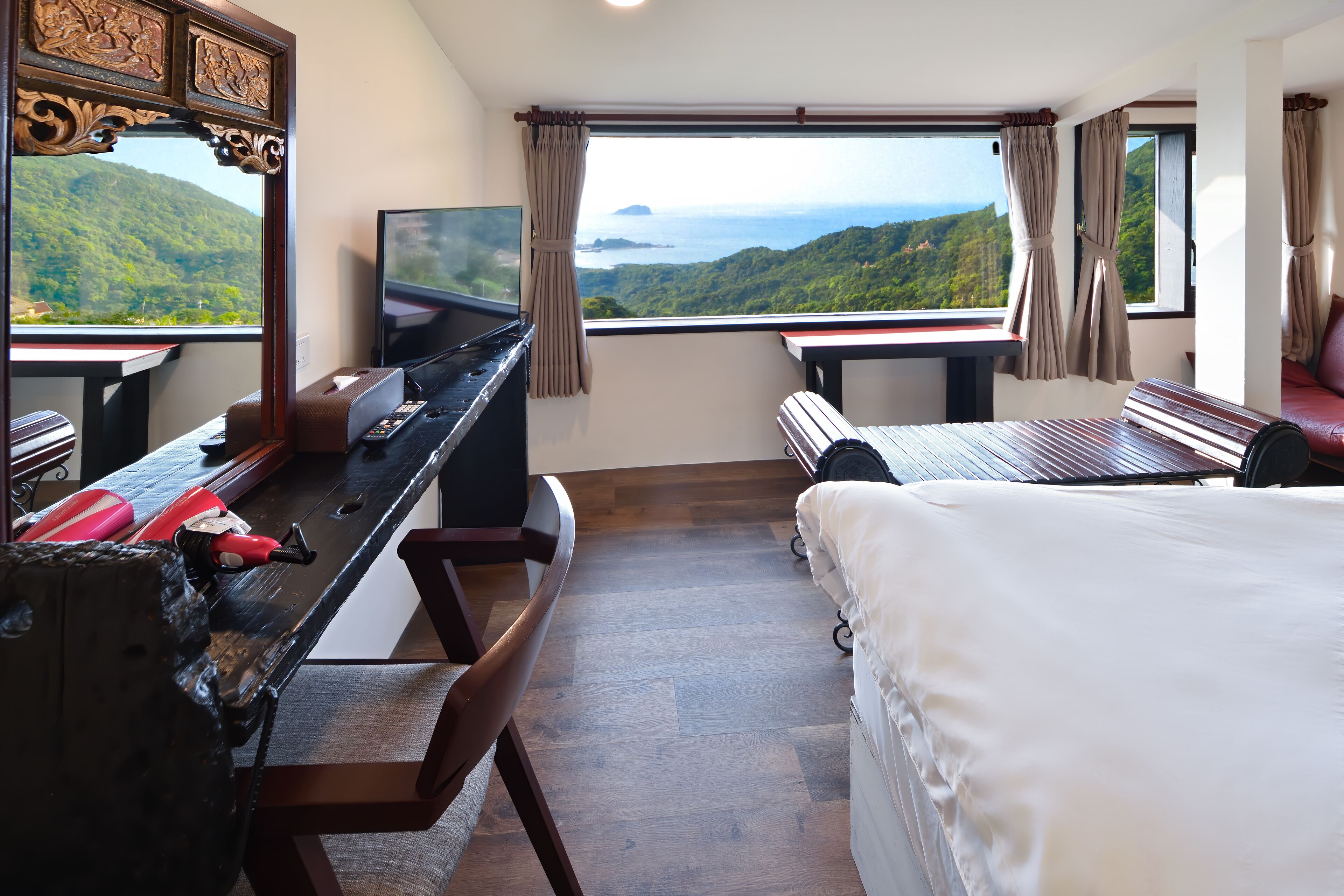 A bedroom with a large bed, a desk with a TV, and a view of a mountainous landscape.