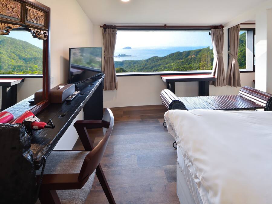 A bedroom with a large bed, a desk with a TV, and a view of a mountainous landscape.