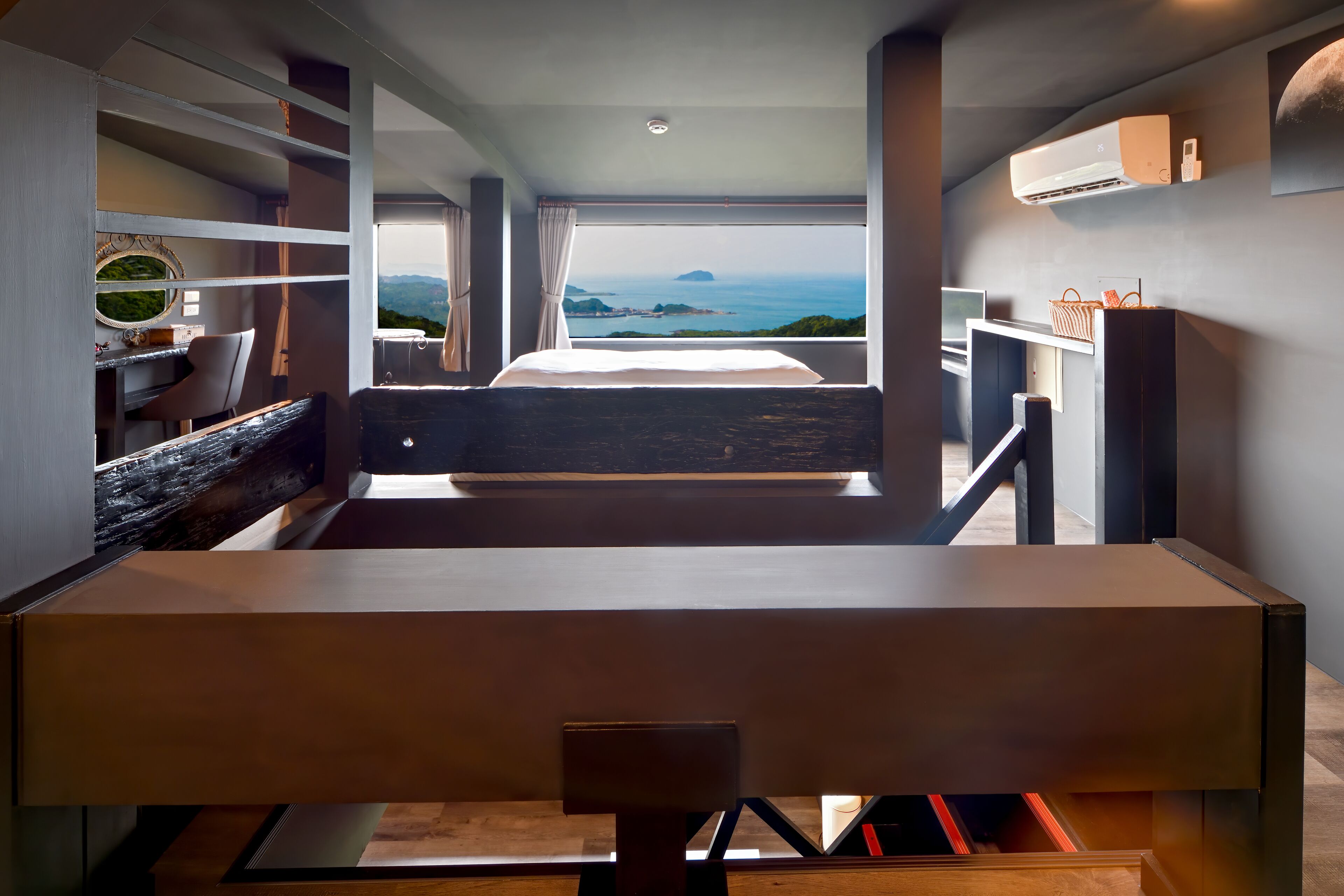 A modern hotel room with a large bed, a desk, and a view of the sea.