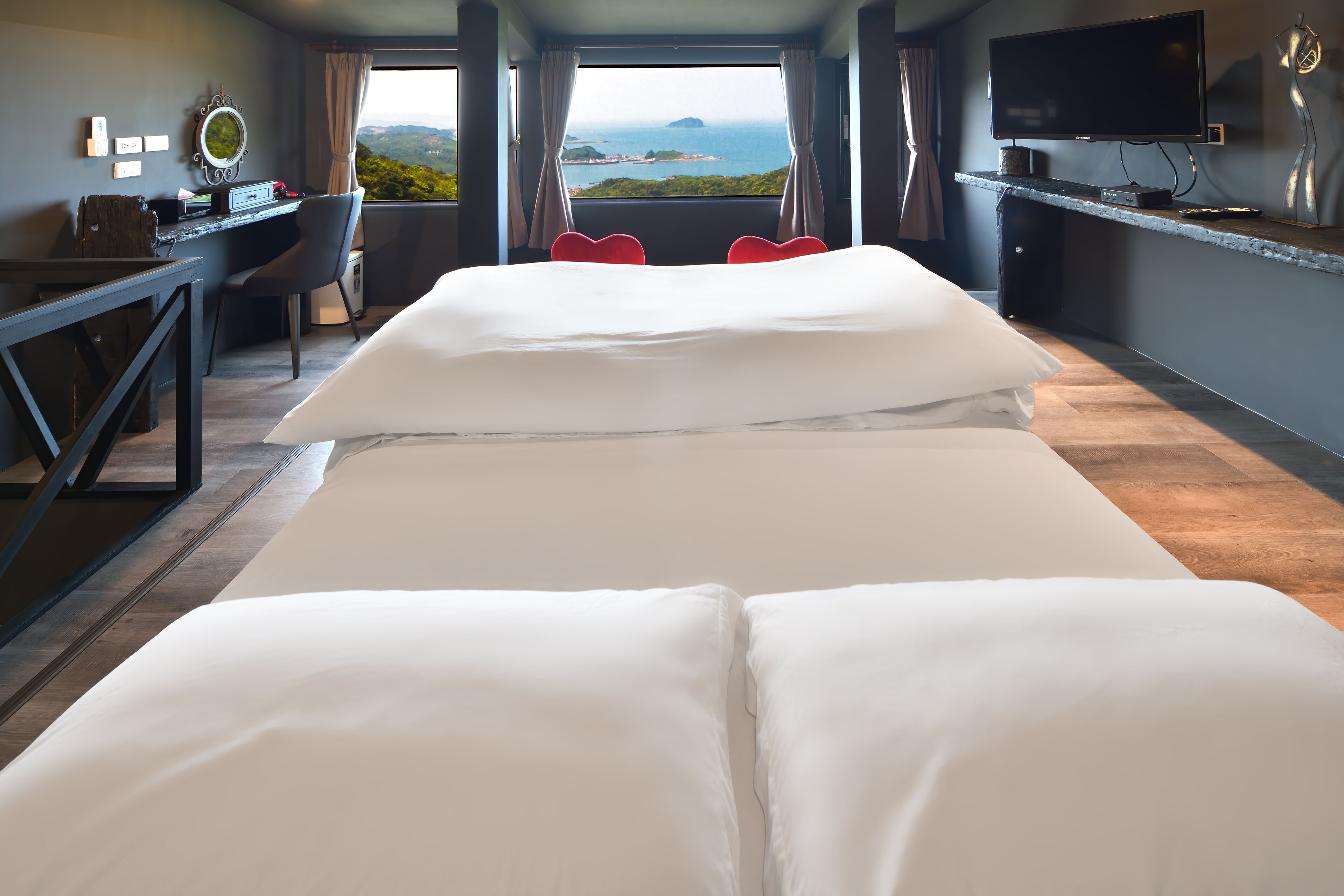 A hotel room with a large bed, a desk with a computer, a TV, and a view of the ocean.