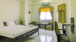 A hotel room with a bed, two chairs, a small table, an air conditioner, and a window with curtains. - Comfy Studio at Menara Kondominium Kelapa Gading Apartment (Jakarta)