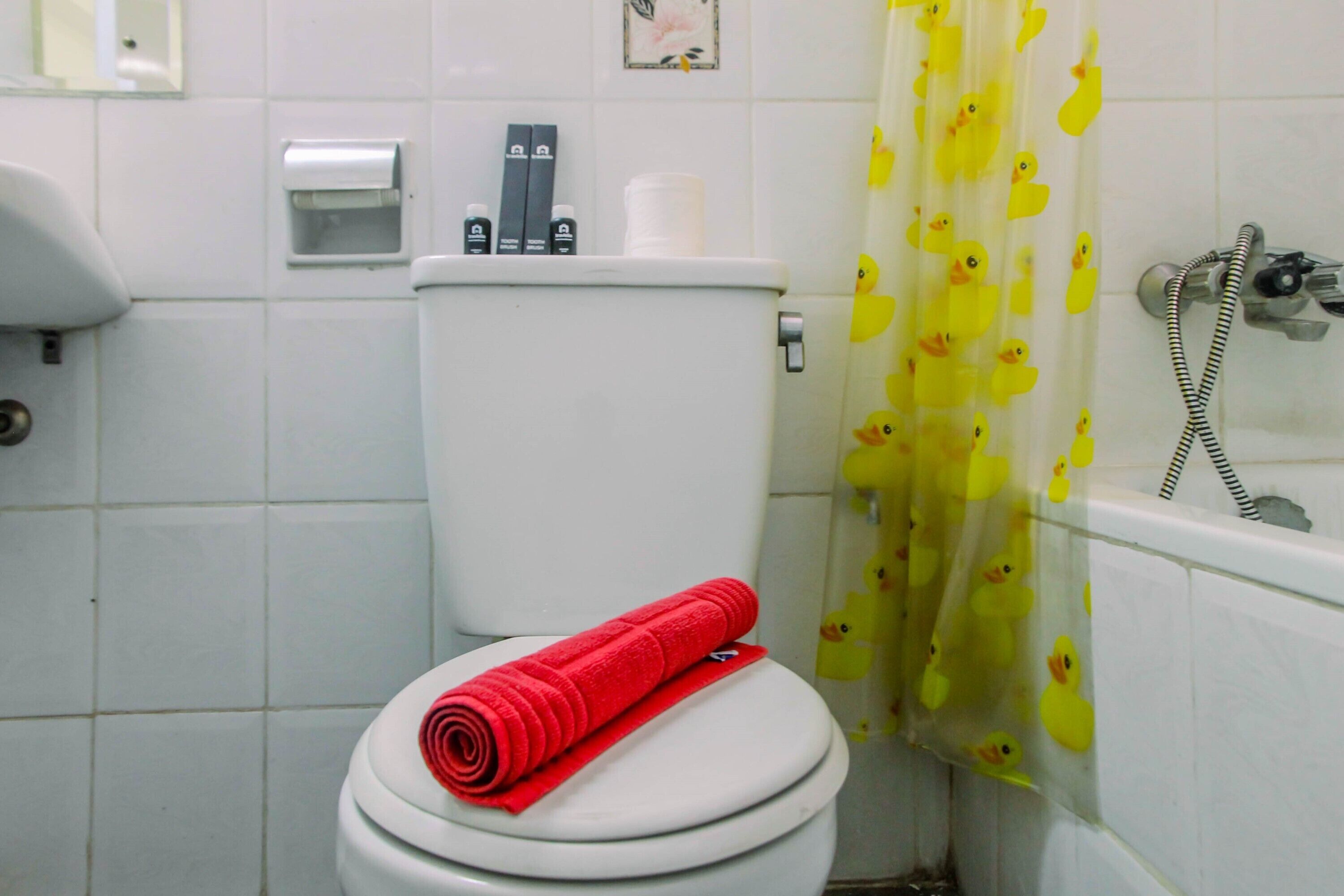 A bathroom with a toilet, a hand dryer, and a shower curtain with duck designs.