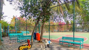 A playground with a checkered floor, benches, a swing set, and a fenced area with trees and flowers. - Comfy Studio at Menara Kondominium Kelapa Gading Apartment (Jakarta)