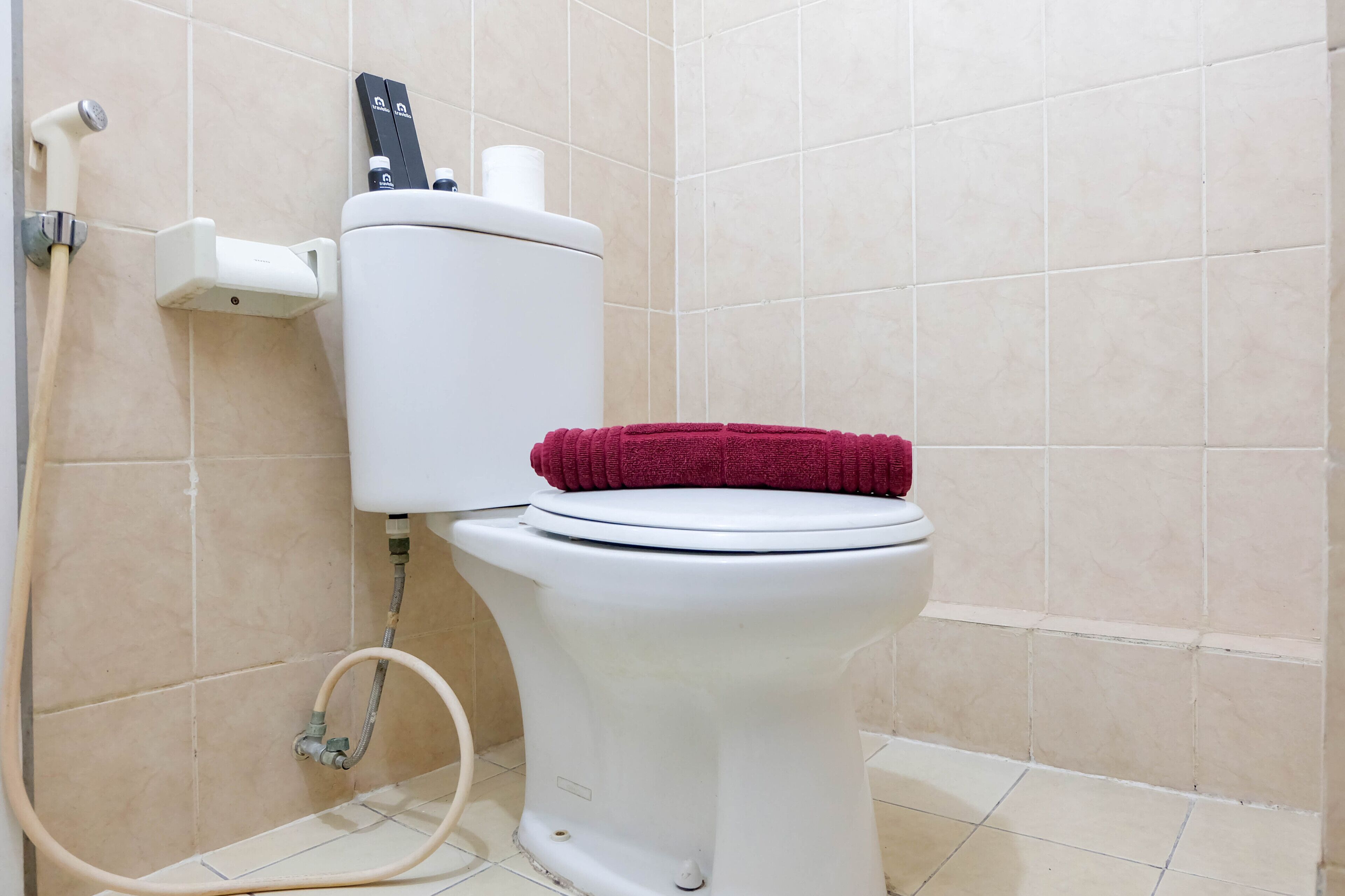 Inodoro blanco con una toalla roja sobre el asiento, un porta papel higiénico y un bidet.