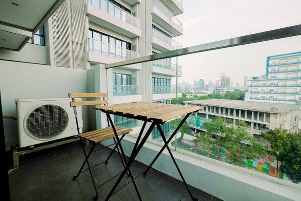 A balcony with a wooden table and chair, an air conditioning unit, and a city view.