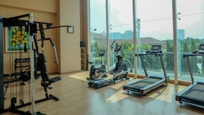 A gym with cardio machines, weight equipment, and large windows offering a city view. - Spacious Studio Room at Capitol Suites Apartment (Jakarta)