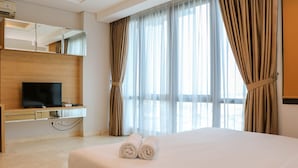 A hotel room with a bed, a TV on a wooden console, a mirror, and sheer curtains. - Spacious Studio Room at Capitol Suites Apartment (Jakarta)