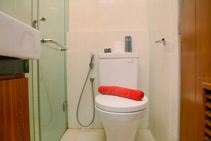 A bathroom with a toilet, a glass shower enclosure, and a wooden door. - Strategic Studio Apartment at Capitol Park Residence (Jakarta)