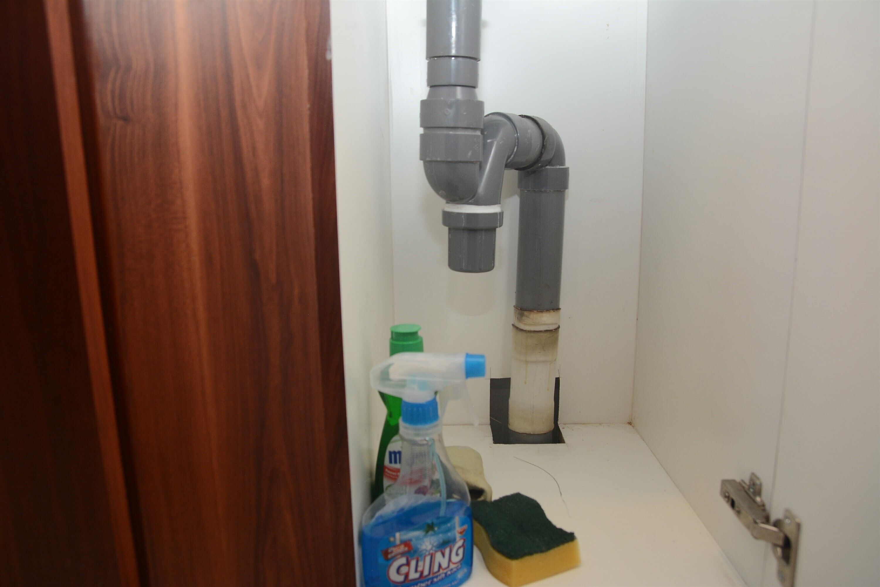 A bathroom with a toilet, a pipe, a bottle of cleaning product, and a sponge.