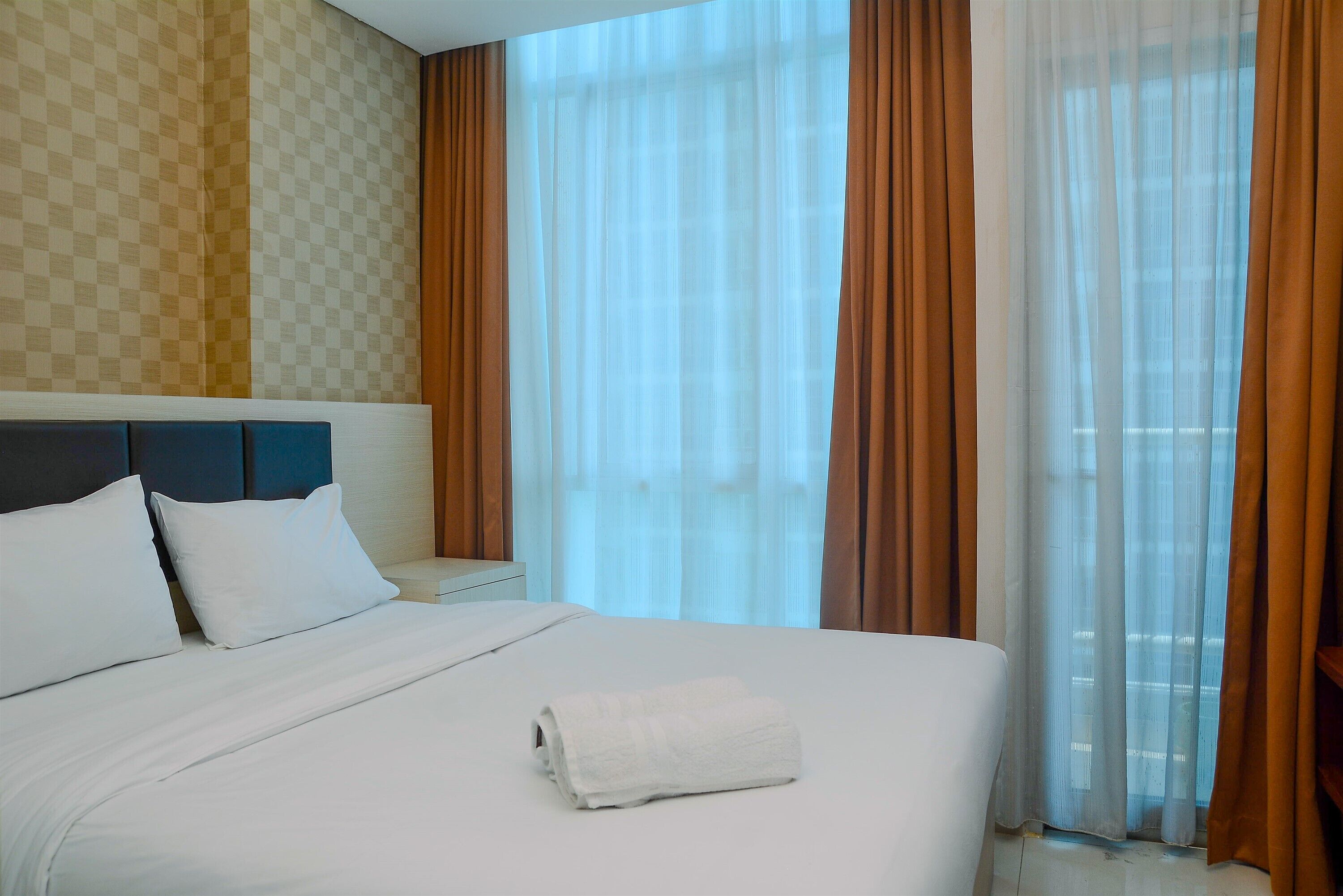 A hotel room with a large bed, white bedding, a headboard, and a view through sheer curtains.