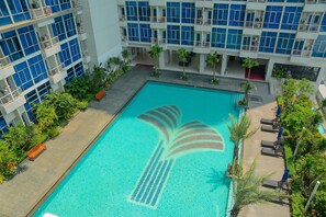 A swimming pool with a palm tree design, surrounded by lounge chairs and palm trees, with a building in the background. - Strategic Studio Apartment at Capitol Park Residence (Jakarta)