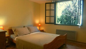 A bedroom with a bed, two bedside tables, a window with a view of trees, and a radiator. - Les Pucines (Six-Fours-les-Plages)
