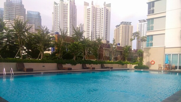 A swimming pool with lounge chairs and a lifebuoy, surrounded by greenery and tall buildings in the background. - Minimalist 2BR Apartment at Springhill Terrace Residence (Jakarta)