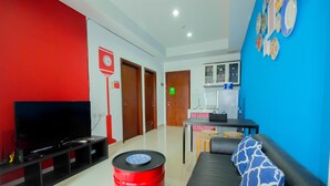 A living room with a flat-screen TV, a red barrel, a black sofa with a patterned pillow, and a blue wall with decorative plates. - Minimalist 2BR Apartment at Springhill Terrace Residence (Jakarta)