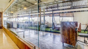 A modern restaurant with a glass partition, outdoor seating, and a view of the construction site. - Hotel Ajmer Regency (Ajmer)