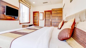 A hotel room with a large bed, a flat-screen TV mounted on the wall, wooden wardrobes, and a window with curtains. - Hotel Ajmer Regency (Ajmer)