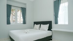 A neatly made bed with white linens and pillows, a dark headboard, and a window with curtains. - Brand New and Modern 3BR Grand Palace Kemayoran Apartment (Jakarta)