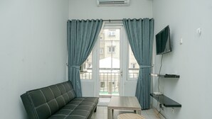 A small living area with a sofa, a table, and a TV mounted on the wall. - Brand New and Modern 3BR Grand Palace Kemayoran Apartment (Jakarta)