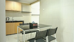 A modern kitchen with wooden cabinets, a black countertop, and a glass dining table with four chairs. - Brand New and Modern 3BR Grand Palace Kemayoran Apartment (Jakarta)