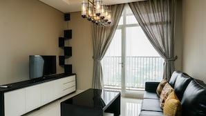 A modern living room with a black sofa, a flat-screen TV, a black coffee table, and a chandelier. - Highest Value 1BR Apartment at Ciputra International (Jakarta)