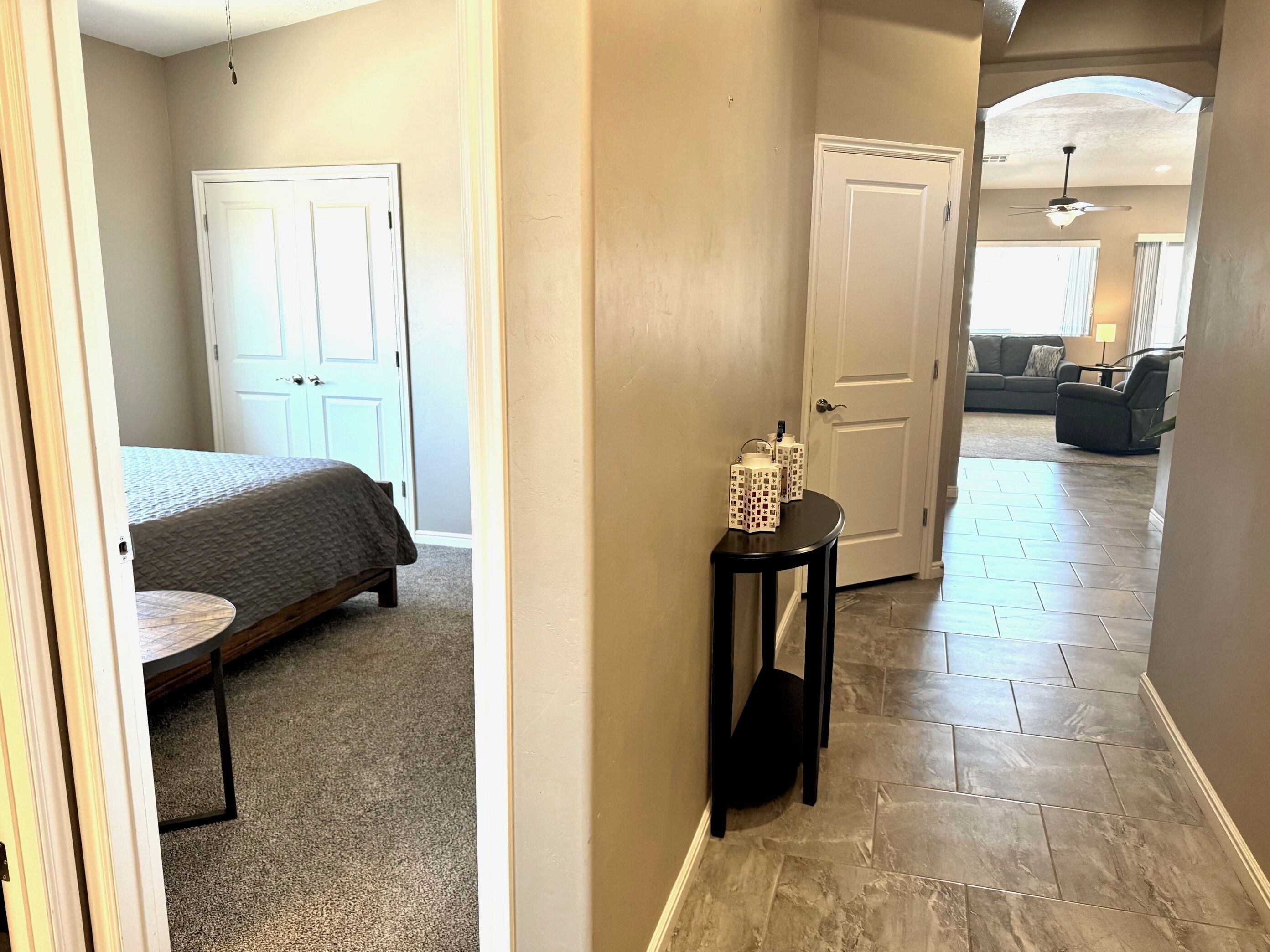 A hallway with a bed, a small table with decorative items, and a door leading to a living area.