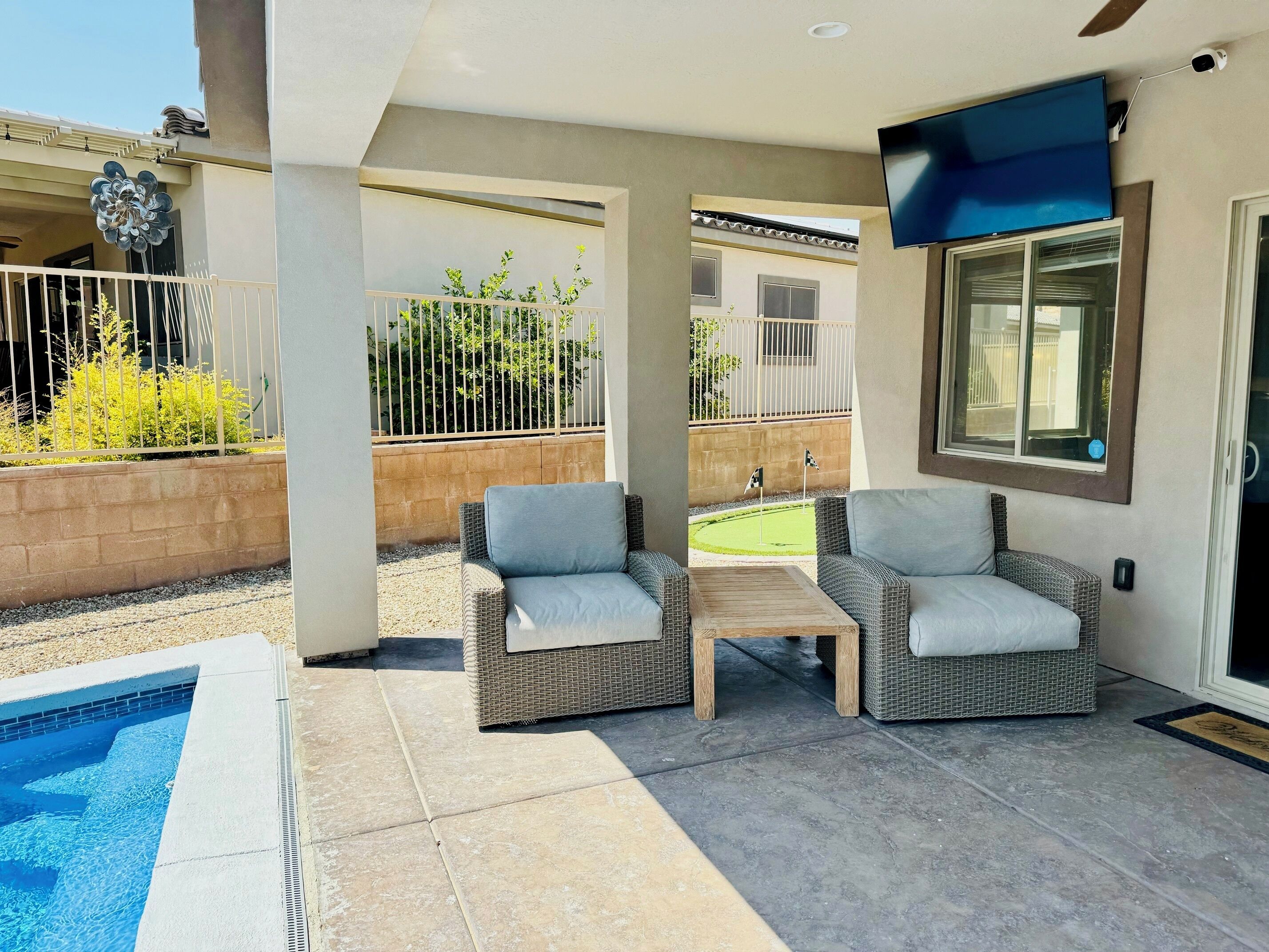 A covered outdoor area with two wicker chairs, a small table, and a pool.