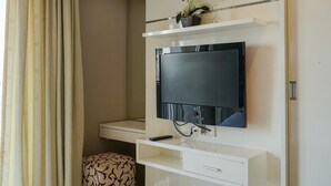 A modern hotel room with a mounted flat-screen TV, a small bedside table, and a decorative plant.