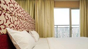 A hotel room with a large bed, a headboard with a red and white pattern, and a view of a balcony with a railing.