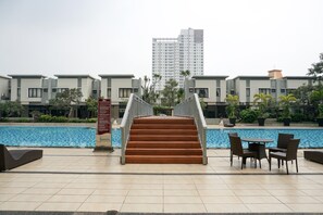 A poolside area with a staircase leading to a building, outdoor seating, and a signboard. - 1BR Apartment at Cosmo Mansion near Grand Indonesia (Jakarta)