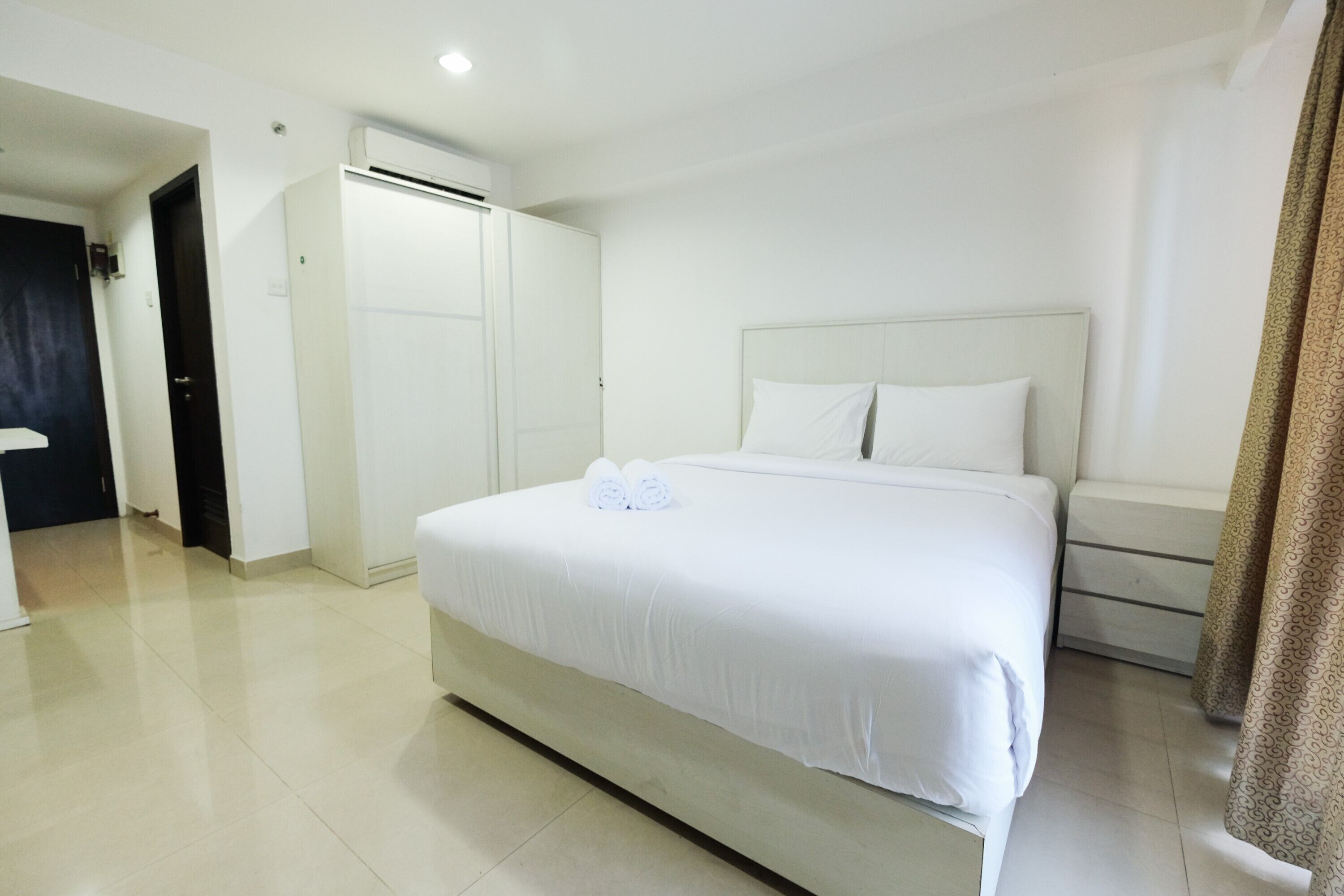 A hotel room with a large bed, a wardrobe, a bedside table, and an air conditioning unit.