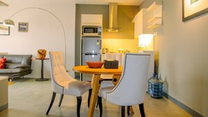A compact living space with a dining area featuring a round table and two chairs, a sofa, a small side table, a microwave, a refrigerator, and a water dispenser.