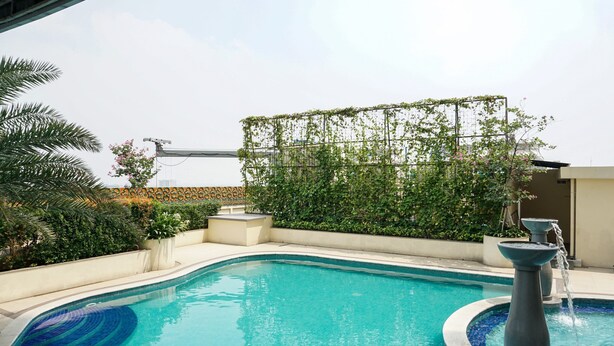 Una piscina con una fuente, rodeada de follaje y una pérgola.