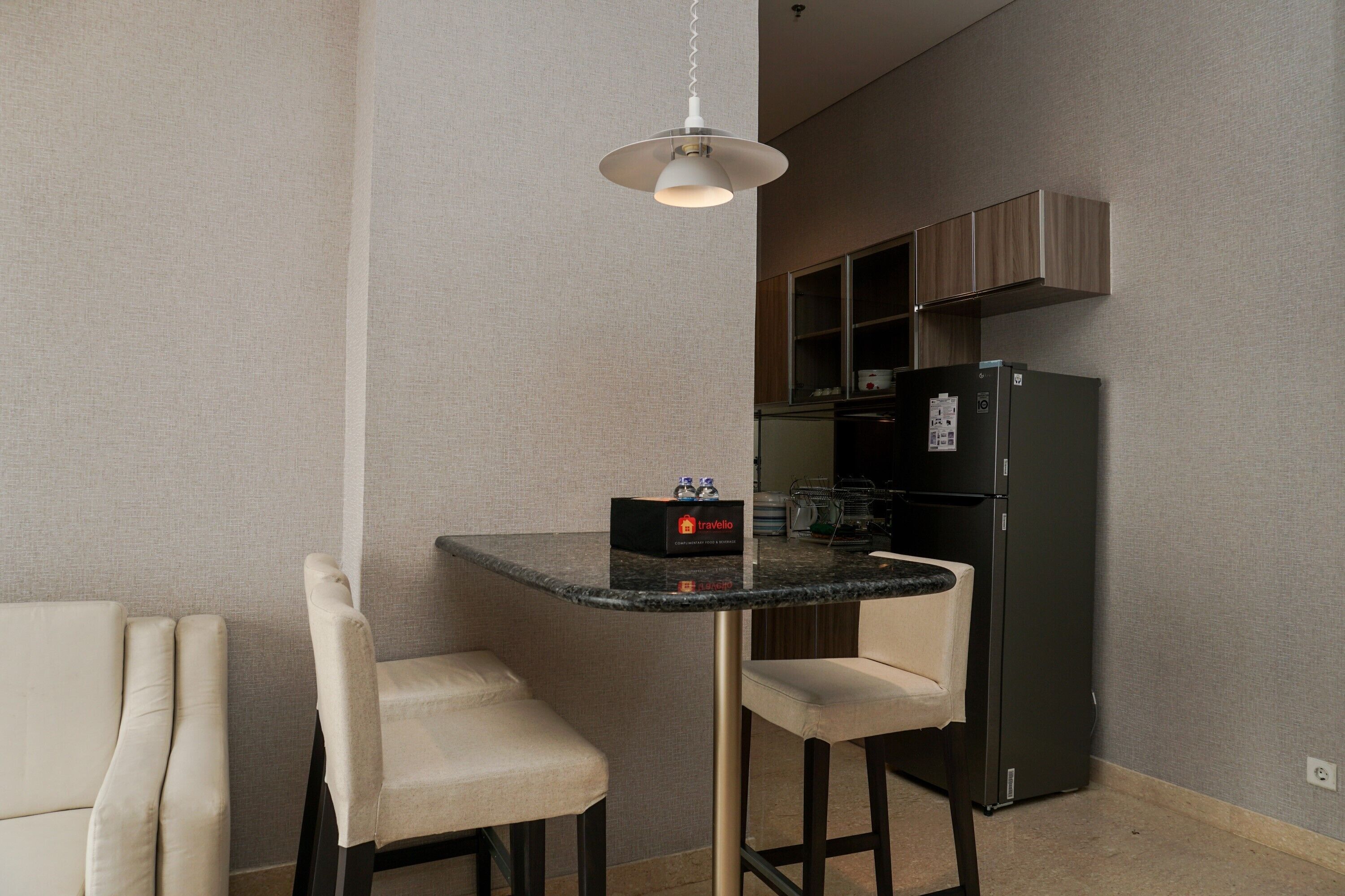 A compact kitchen with a black refrigerator, a small island table with two chairs, and a pendant light.